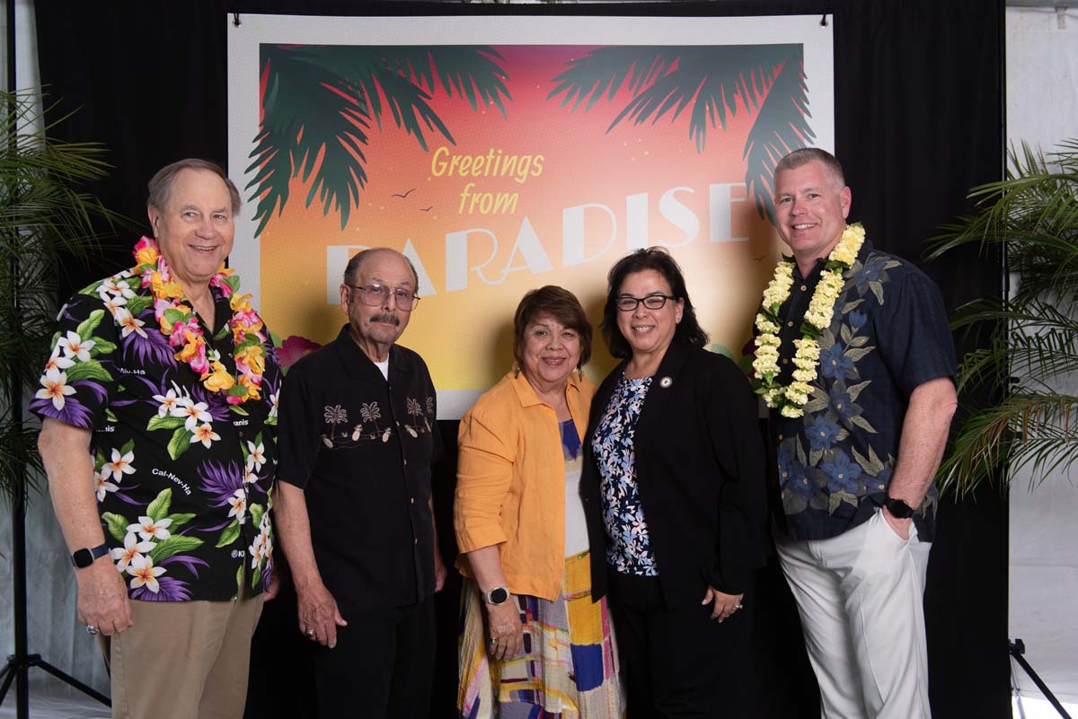 Five people in front of Greetings from Paradise sign