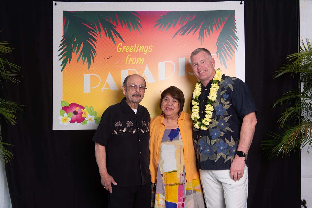 Three people in front of Greetings from Paradise sign