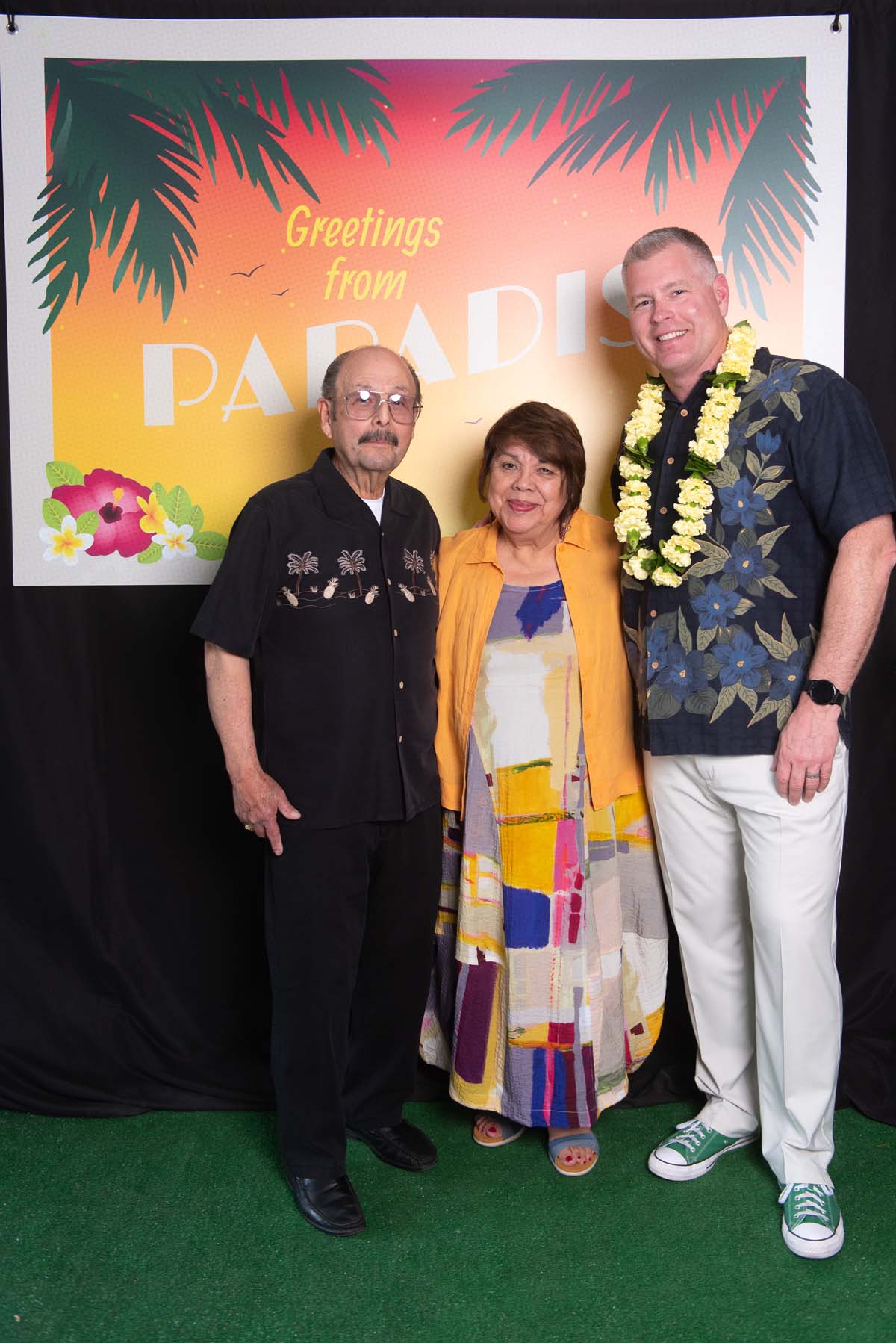 Three people in front of Greetings from Paradise sign