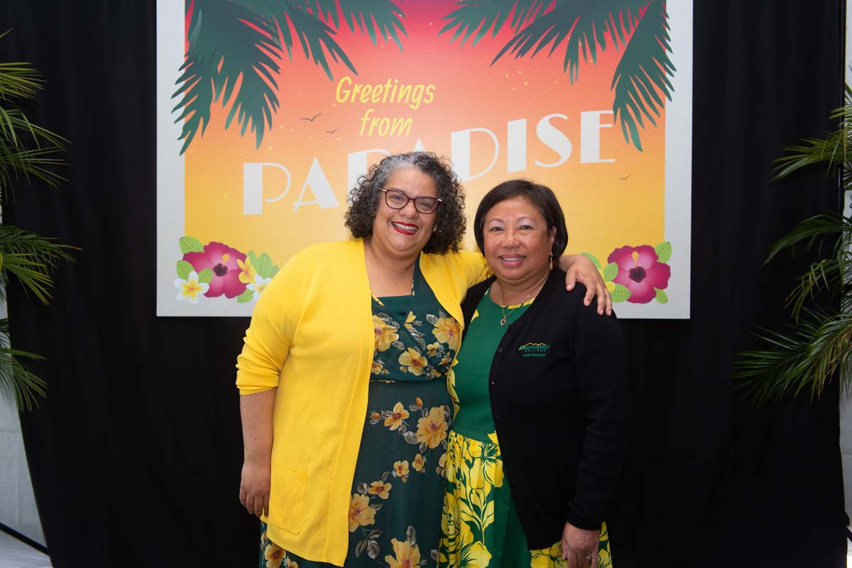 Two people in front of Greetings from Paradise sign