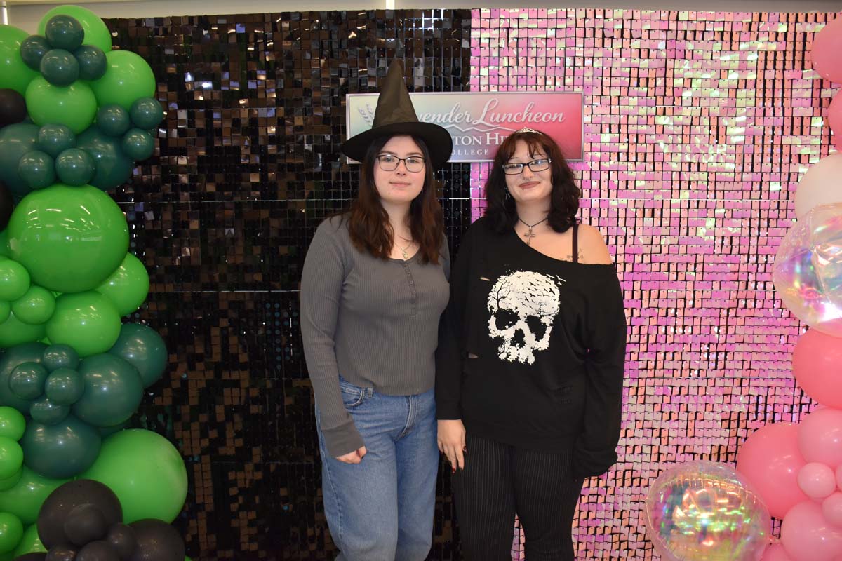 Two students posing in front of a Wicked backdrop