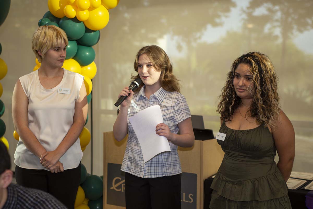 Three students standing at the front with a microphone