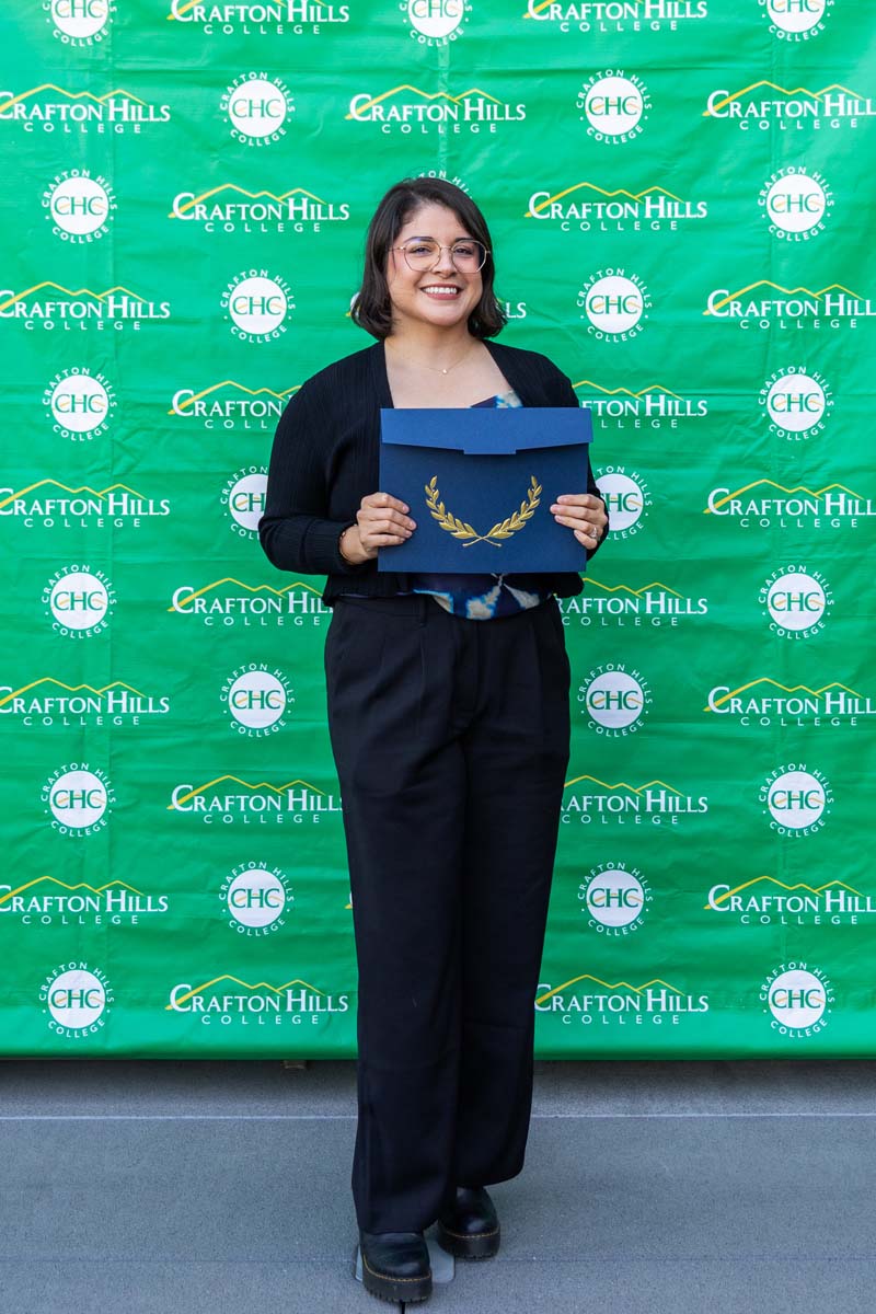 Student holding certificate in front of backdrop